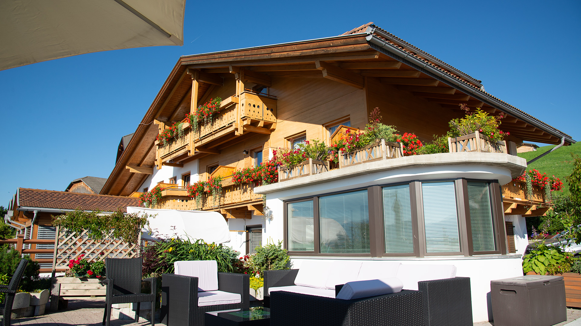 Die Pension Wiesenrain in Meransen, mit blumengeschmückten Balkonen und einer möblierten Außenterrasse zum Entspannen.