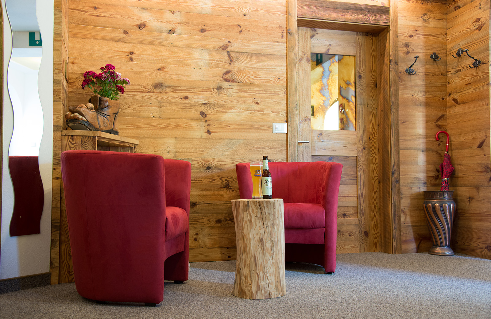 Cozy living room in Tyrolean rustic style with wooden walls, red armchairs, and a log coffee table.