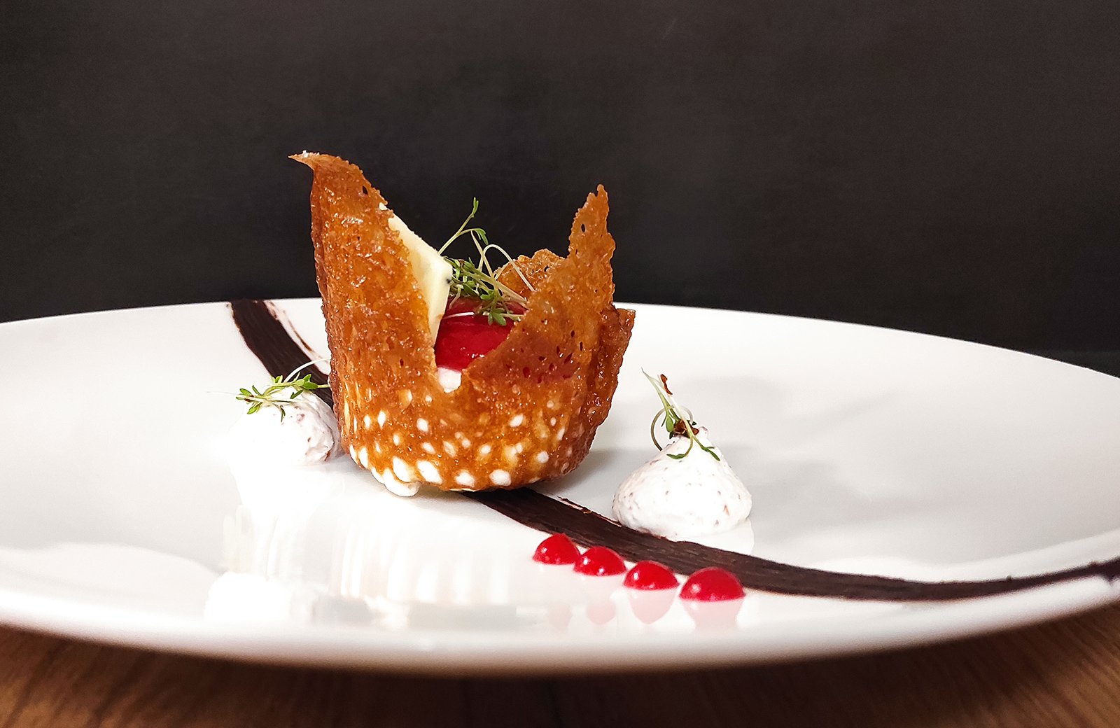 Ein Gourmet-Dessert aus der Küche der Pension Wiesenrain, mit knuspriger Waffel, roten Früchten, Sahne und Dekorationen.