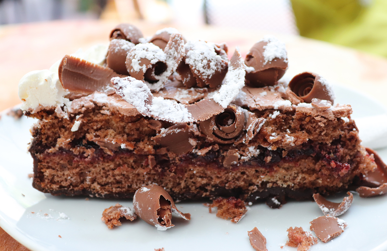 Ein Stück Schokoladenkuchen mit Beerenfüllung, dekoriert mit Schokoladenlocken und Puderzucker, ein Beispiel unserer Südtiroler Küche.