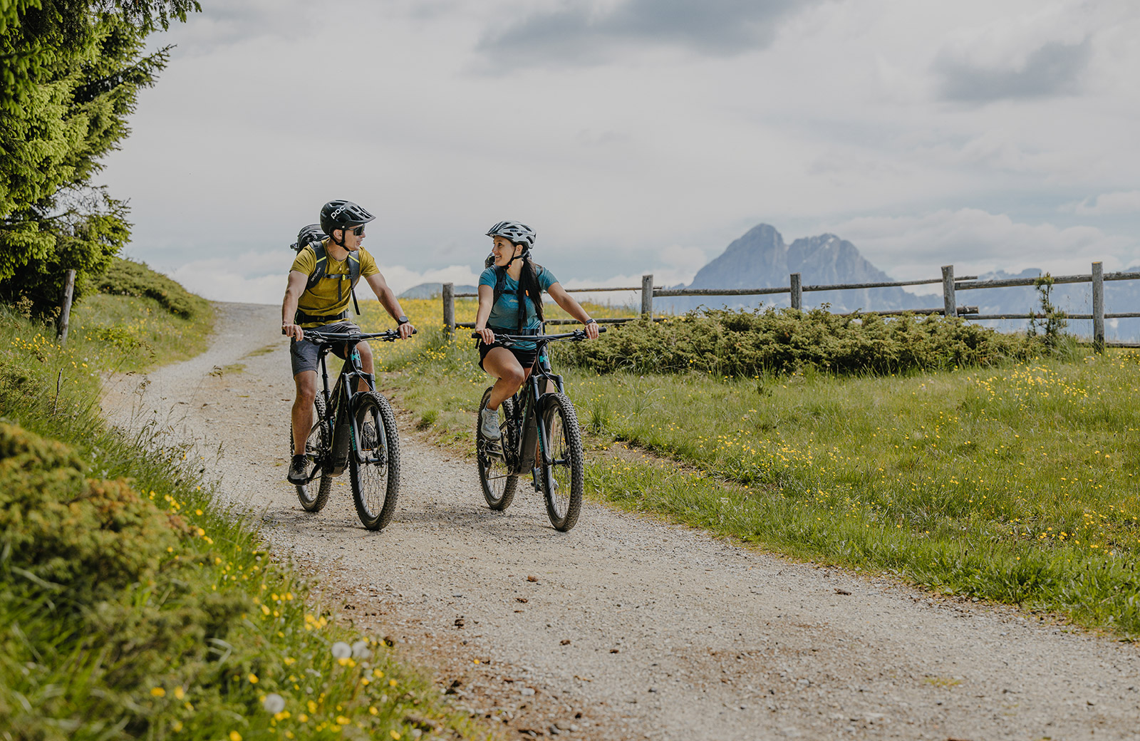 Couple on mountain bikes on a dirt path in Maranza, with the Dolomites in the background, ideal for summer excursions.