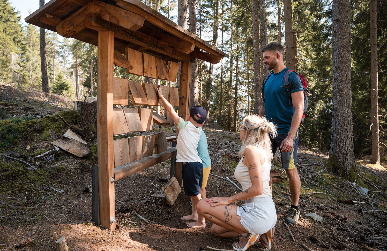 Happy family hiking in Maranza, Pusteria Valley, interacting with a wooden game in the forest.