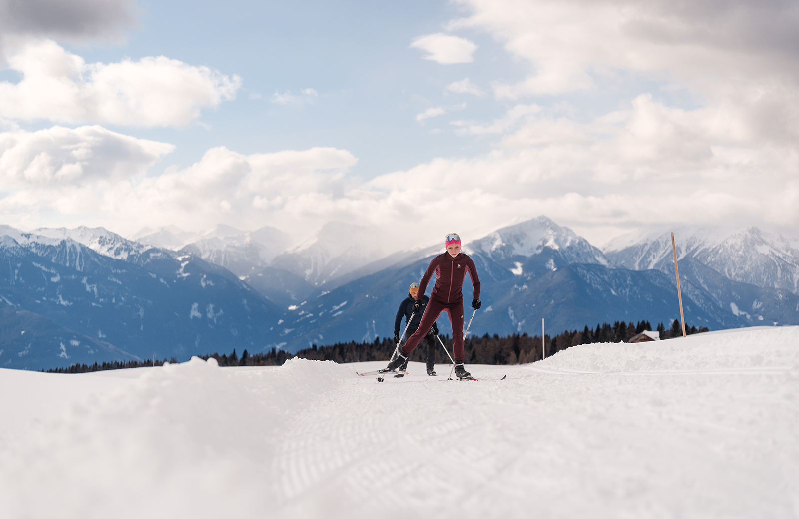 Two people skiing on the snow in Maranza, with the Dolomites and Val Pusteria in the background.