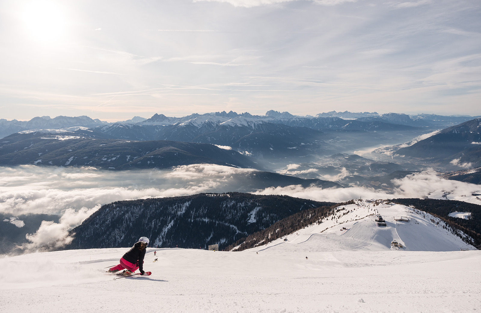 Breathtaking winter scene in Meransen: A skier in pink descends a snowy slope, with the Dolomites and Pustertal shrouded in fog in the background.
