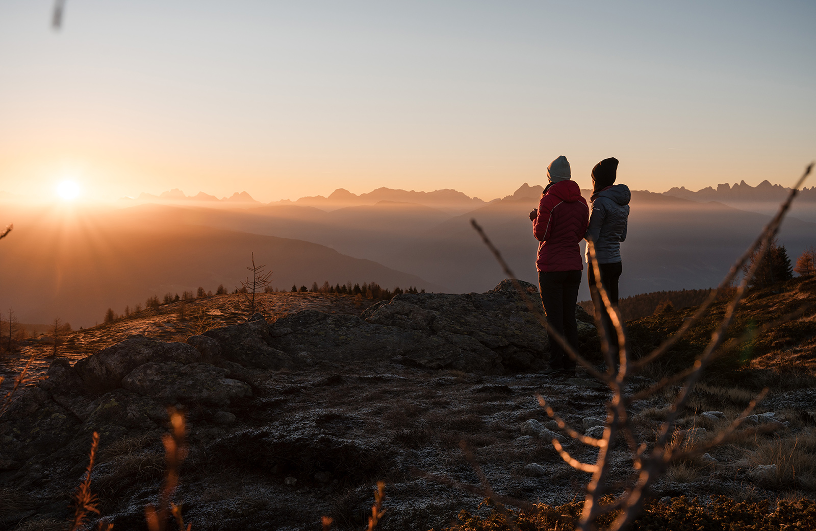 Two hikers admire the sunset over the Dolomites and the Puster Valley from Maranza, South Tyrol.
