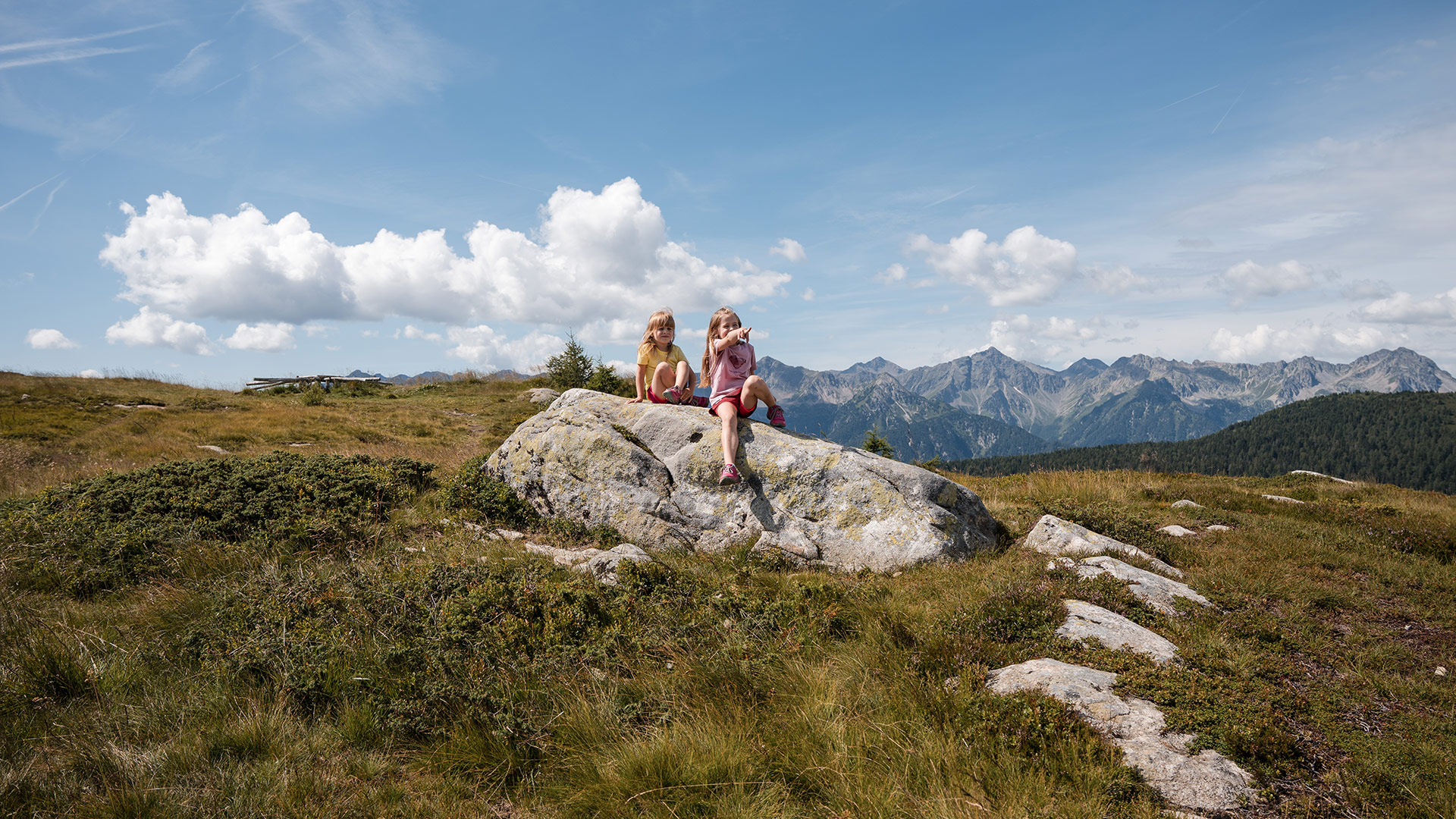 Zwei lächelnde Mädchen genießen die Aussicht auf die Dolomiten während einer Sommerwanderung in Meransen.