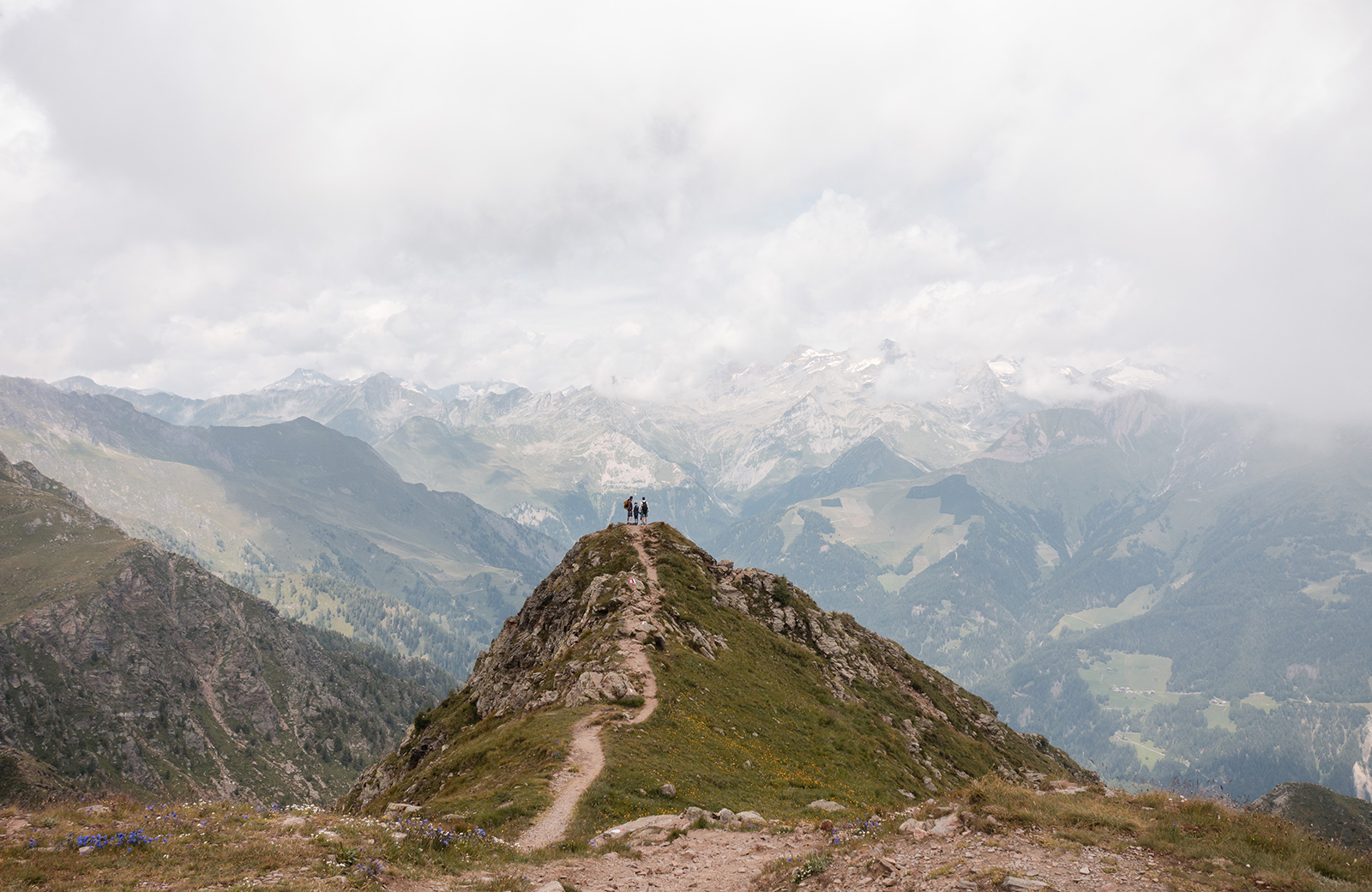 Three hikers on a rocky trail on Gitschberg, with a view of the Dolomites and Puster Valley.