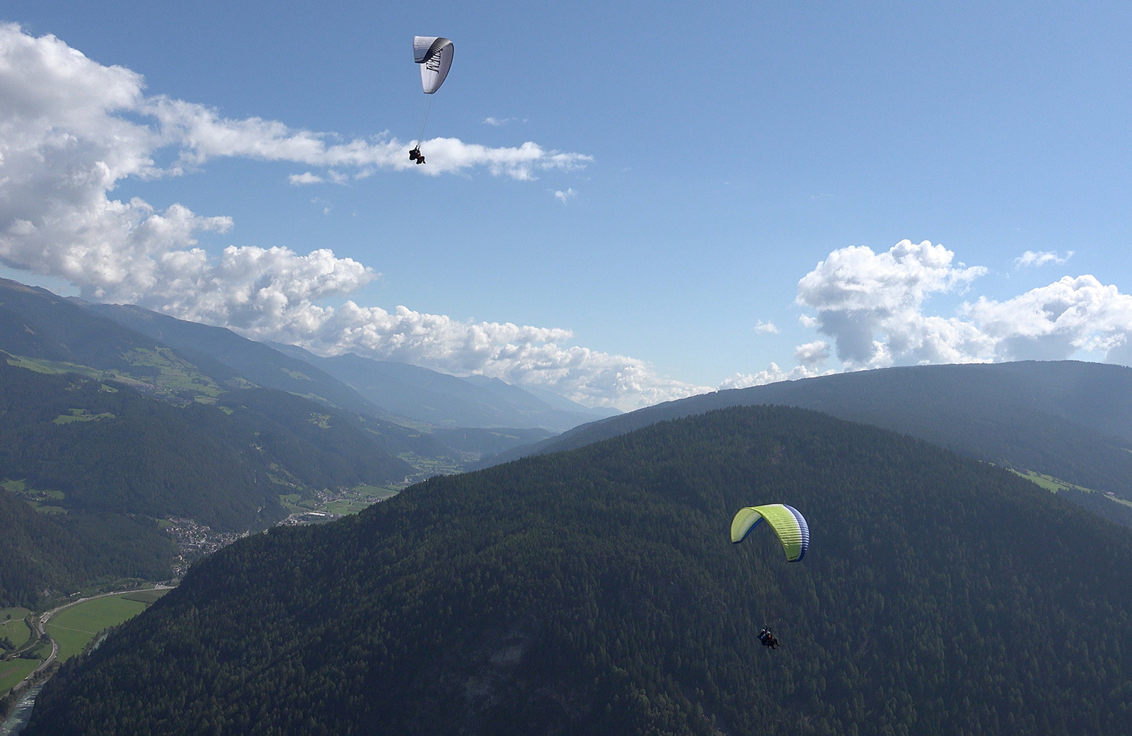 Two paragliders fly over the green valleys and mountains of South Tyrol, with a spectacular view of the Pusteria Valley.