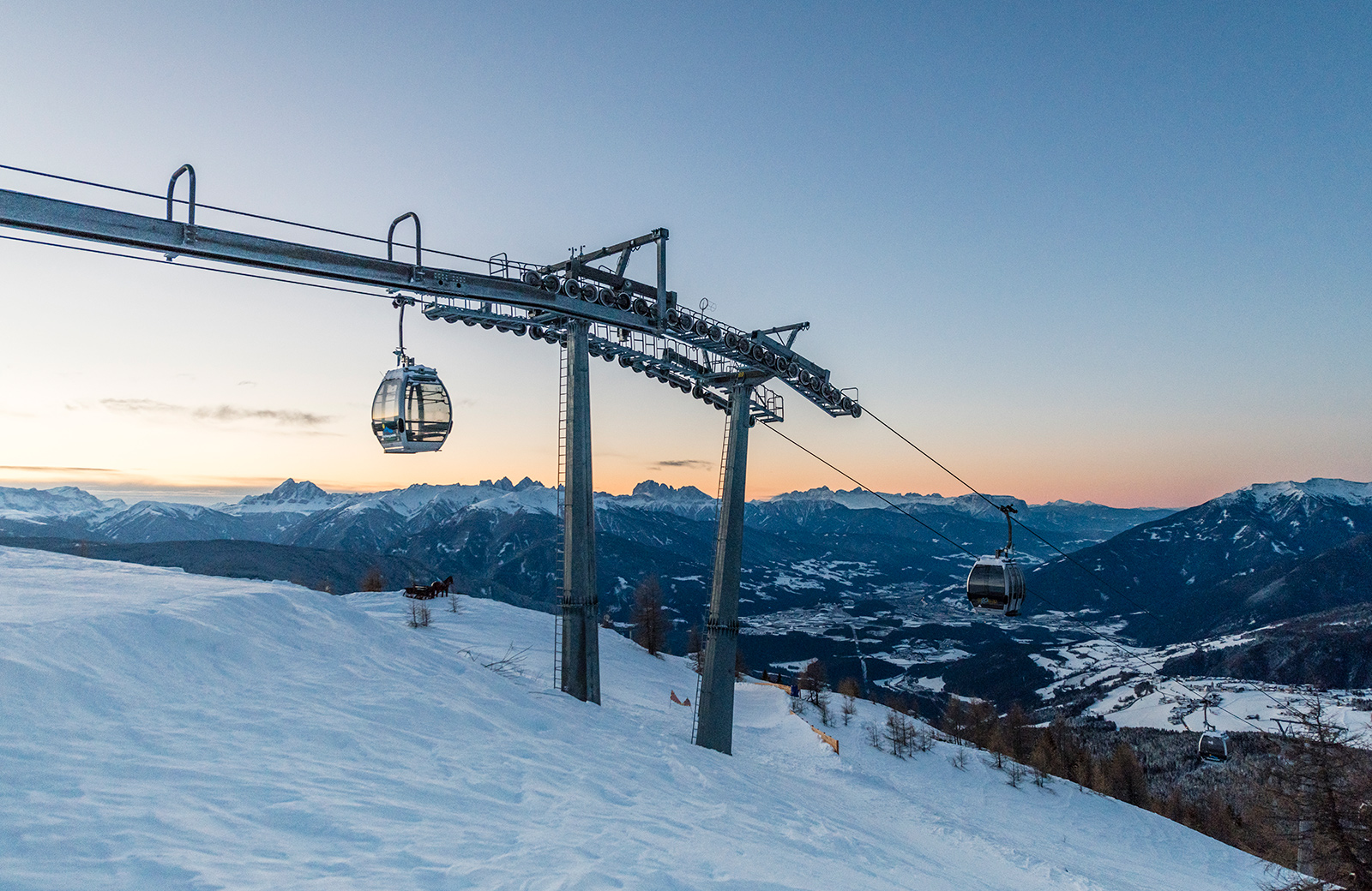 Gitschberg-Jochtal cable car cabins above snow-covered slopes at sunset, with a view of the Pusteria Valley.