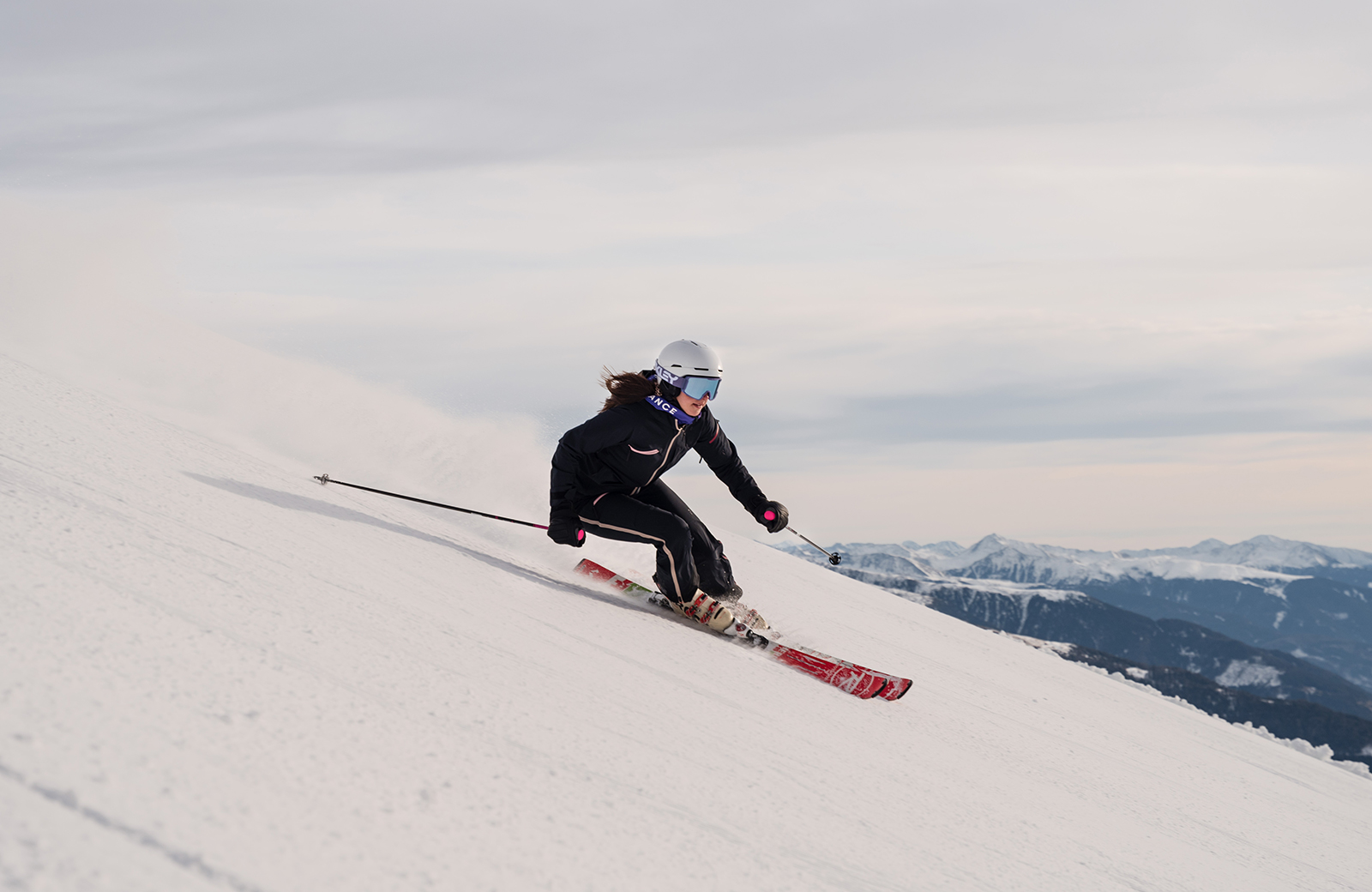 A smiling skier in a black suit descends a snowy slope in the Gitschberg Jochtal ski area, with the Dolomites in the background, enjoying a ski holiday in Maranza.